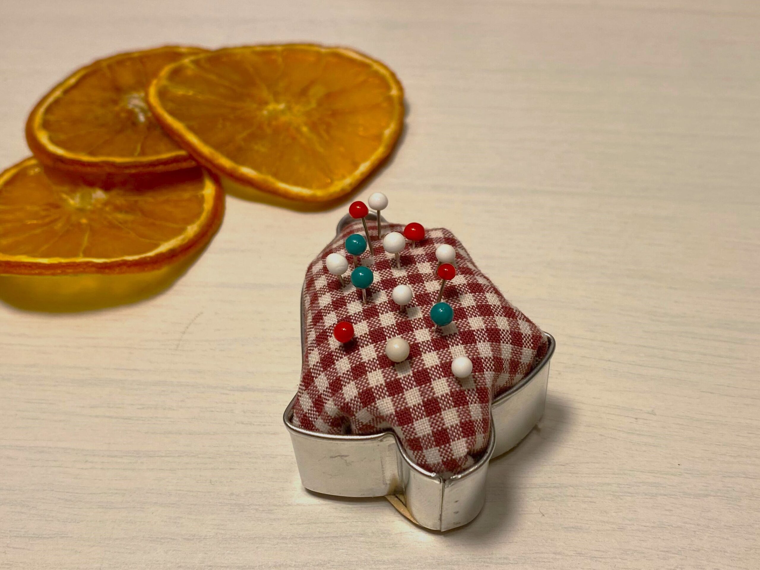 Geschenkidee aus einem Plätzchenausstecher der mit einem rot-weiß kariertem Stück Stoff zu einem Nadelkissen umfunktioniert wurde.