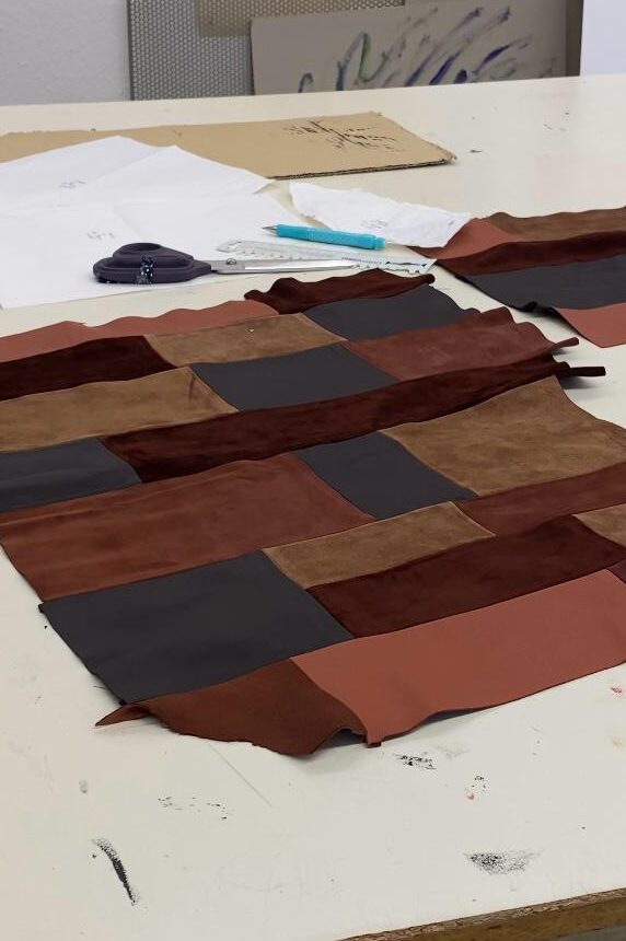 Atelier Arbeitstisch mit Lederstücken in verschiedenen Braun-tönen. Zeichnungen im Hintergrund